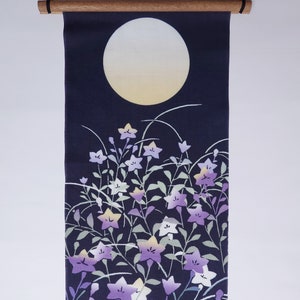 May include: A dark blue fabric wall hanging featuring a white moon and a design of purple and white flowers with green leaves. A small white rabbit is in the bottom right corner.