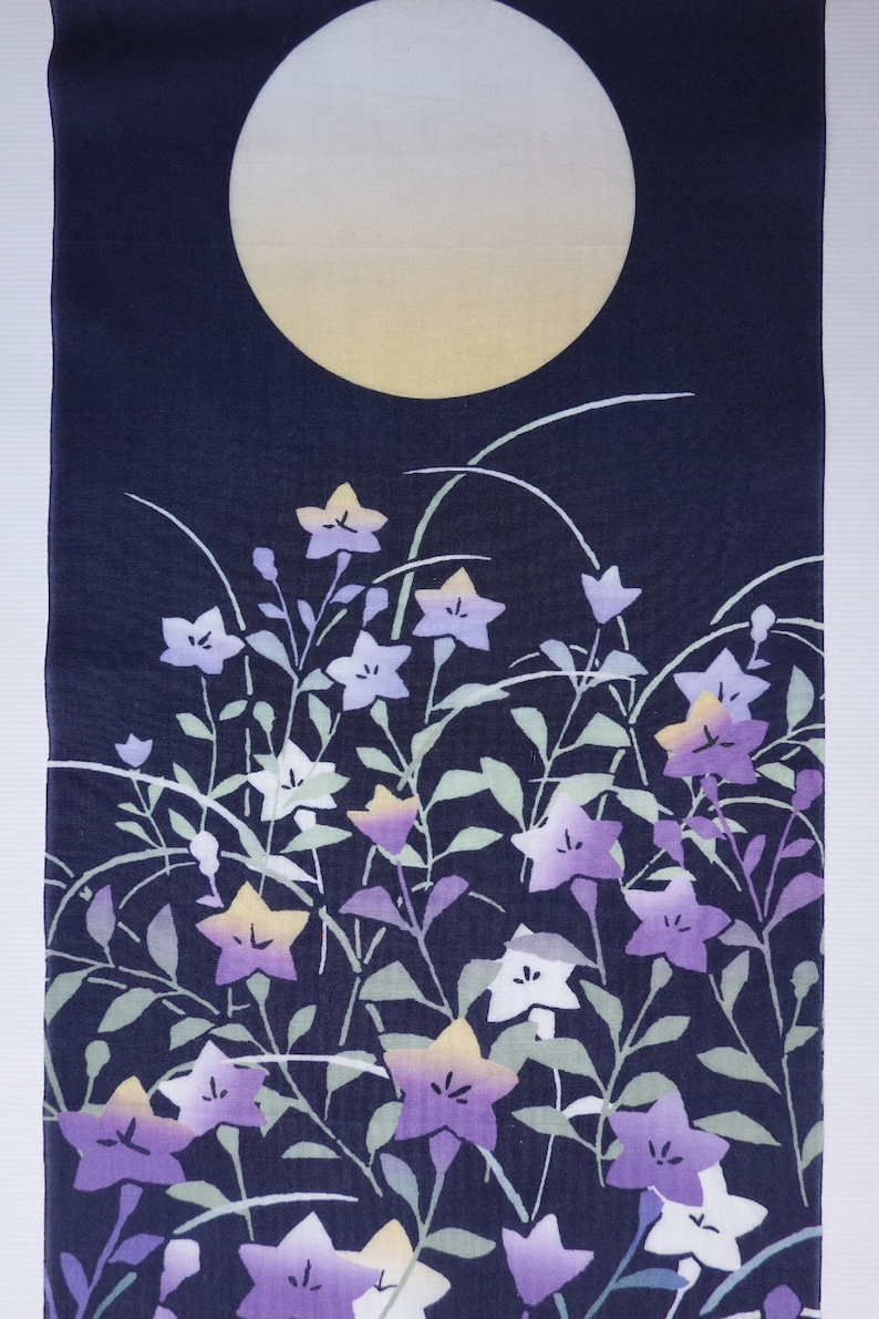 May include: A dark blue fabric with a white moon and a pattern of purple and white flowers on green stems.