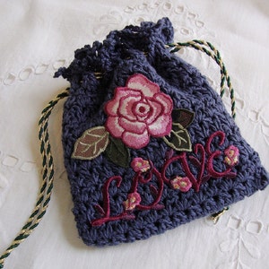 May include: A small, dark blue crocheted drawstring bag with a pink embroidered rose and the word "Love" in red embroidery.