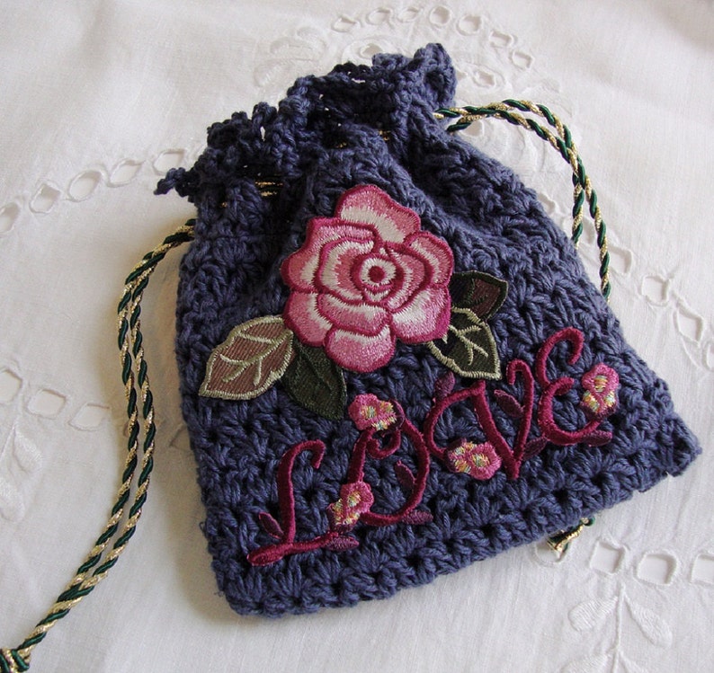 May include: A small, dark blue crocheted drawstring bag with a pink embroidered rose and the word "Love" in red embroidery.