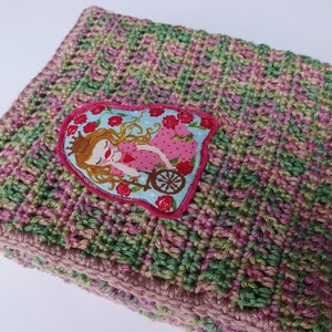 May include: A crocheted baby blanket in shades of pink and green with a heart-shaped applique featuring a princess in a carriage.