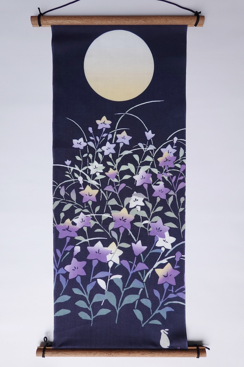 May include: A dark blue fabric wall hanging featuring a white moon and a design of purple and white flowers with green leaves. A small white rabbit is in the bottom right corner.