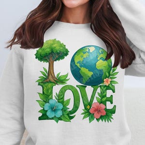 May include: White sweatshirt featuring a green tree, a blue and green globe, and the word "LOVE" in green letters. The globe and letters are surrounded by green leaves and pink flowers.