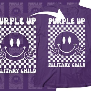Op de afbeelding: Paars T-shirt met een wit geruit patroon en een smiley met vredestekens. De tekst "Purple Up Military Child" is op het shirt gedrukt.