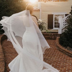 May include: A floor-length off-white or pure white wedding veil with a scalloped edge, measuring 274.32 cm in length. The veil is sheer and lightweight, featuring a delicate pattern along the border, shown with feedback from Ellen Peters.
