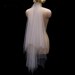 May include: A two-tier white tulle wedding veil featuring a scalloped edge with delicate bead accents. The veil is attached to a floral headpiece composed of small cream and pale yellow fabric flowers, displayed on a mannequin torso.