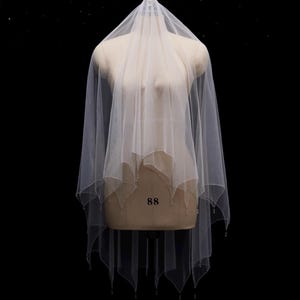 May include: A white, sheer, multi-layered wedding veil featuring a scalloped edge design. The hem of the veil is adorned with small, delicate beads that hang from each point of the scalloped fabric, creating a subtle, decorative finish.