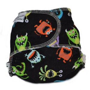 May include: A black cloth diaper with a colorful monster print. The diaper has a white elastic waistband and a white trim around the edges.