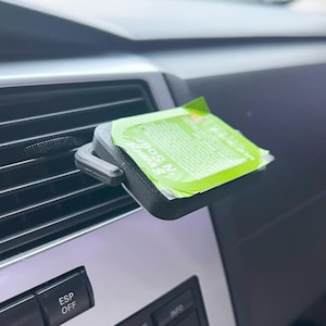 May include: A black plastic car air vent clip with a green air freshener attached. The air freshener has the text "N' SOiL" printed on it.