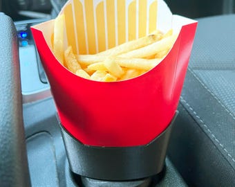 May include: A red and yellow paper container filled with golden french fries, placed in a black car cup holder. The container has a red exterior and a yellow and white interior design.
