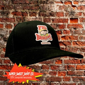 May include: Black mesh trucker hat with a red, white and yellow logo that says "Pig Burgers" with a cartoon pig wearing a sombrero. The logo also says "Everybody makes 'em, we make 'em good" and "Greendale, CA".