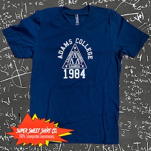 Könnte beinhalten: Ein marineblaues T-Shirt mit einem weißen Aufdruck eines Dreiecks mit den Worten "Adams College" und "Lambda 1984" darin.