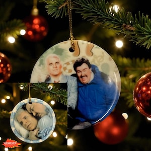 May include: Round ceramic Christmas ornament featuring images of actors. The ornament has a gold string for hanging. The background is a festive scene with a Christmas tree and red ornaments. The ornament is a unique holiday decoration.