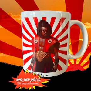 May include: White ceramic mug with a red and white rising sun design. The mug features a black man in a red and gold costume with a sword. The text "SUPER SWEET SHIRT CO. 100% Screenprinted Awesomeness." is at the bottom of the mug.