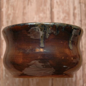 May include: A brown ceramic bowl with a dark glaze and a slight iridescent sheen. The bowl has a rounded bottom and a flared rim.