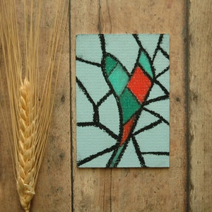 May include: A small, framed artwork with a colourful abstract design. The design features a red, green and blue geometric pattern on a light blue background.