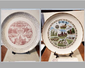 May include: Two vintage souvenir plates featuring images of Iowa. The first plate is red and white with a gold rim and features the state capitol building. The second plate is white with a gold rim and features a colorful illustration of the state seal, a covered wagon, a cornfield, and other Iowa landmarks. Both plates are on display stands.