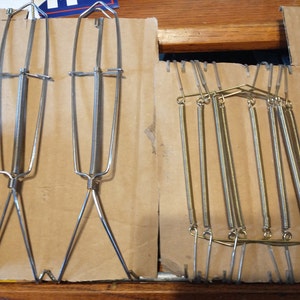 May include: Two silver spring-loaded garment hangers and a set of six gold spring-loaded garment hangers on a brown cardboard background.