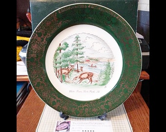 May include: A white ceramic plate with a green and gold rim. The plate features a scenic illustration of a lake with trees and deer, with the text "White Swan State Park, Ill." at the bottom.