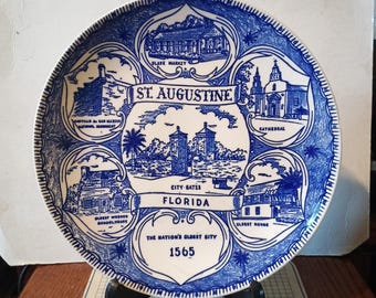 May include: A decorative blue and white plate featuring illustrations of St. Augustine, Florida landmarks. The plate includes text that reads "St. Augustine, Florida" and "The Nation's Oldest City 1565".