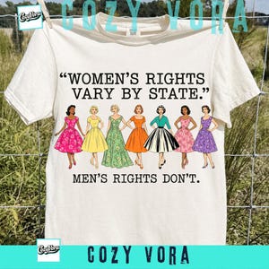 Puede incluir: Una camiseta de manga corta color crema con el texto en negro "WOMEN'S RIGHTS VARY BY STATE." y "MEN'S RIGHTS DON'T." junto a una ilustración gráfica de siete figuras diversas con vestidos coloridos de estilo vintage en fila.