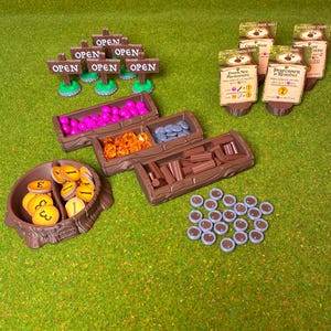 Puede incluir: Un juego de mesa con varios componentes. Incluye bandejas de madera llenas de piezas de juego rosas, naranjas y grises, fichas de madera y pequeños letreros de madera que dicen "OPEN". También incluye cartas de juego y fichas redondas.