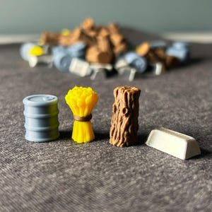 Op de afbeelding: Vier miniatuur spelstukken: een blauwe metalen ton, een gele bundel tarwe, een bruine houten boomstam en een zilveren staaf.