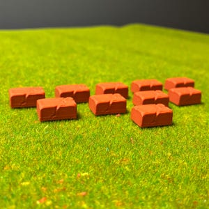 May include: A cluster of small, brick-red rectangular objects, possibly miniature building blocks or decorative elements. They are arranged on a vibrant green surface, creating a contrast of colours and textures. The objects have a textured surface, suggesting a brick-like appearance.