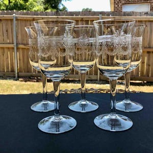 May include: Set of six clear glass wine glasses with a delicate etched design. The glasses have a tall, slender stem and a wide bowl.