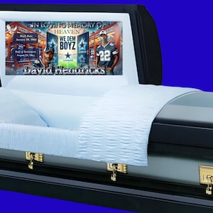 Può includere: Una bara blu e argento con finiture dorate. Il coperchio è aperto e all'interno c'è una coperta bianca. Il coperchio ha un'immagine stampata di un giocatore di football e il testo "In Loving Memory of Heaven We Dem Boyz David Neulucks".