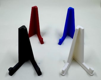 Op de afbeelding: Vier kleine display stands in zwart, rood, blauw en wit. Elke standaard heeft een driehoekige vorm met een basis en een kleine richel om een item vast te houden. De stands zijn gemaakt van een solide materiaal en zijn ontworpen om kleine items vast te houden.