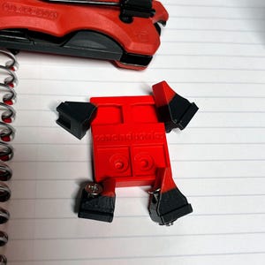 May include: Red and black tool with the text "cone industries" and a red multi-tool. The tool has a rectangular body with black appendages and is attached with screws. The multi-tool is red and black.