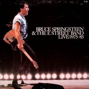 Puede incluir: Portada del álbum Bruce Springsteen y la E Street Band Live 1975-85 con una foto en blanco y negro de Bruce Springsteen tocando la guitarra en un escenario con una fila de luces de escenario detrás de él.