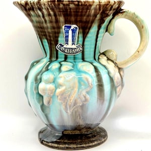 May include: A vintage ceramic pitcher with a turquoise, brown, and gray glaze. The pitcher features a decorative handle and a detailed embossed design. The Bay Keramik label is visible on the front. A unique piece for home decor.