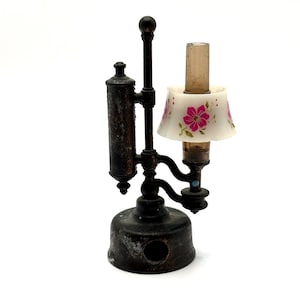 May include: A miniature antique lamp with a dark bronze finish. The lamp features a small lampshade with a floral pattern in pink and white. The lamp is a decorative item, likely for a dollhouse or display.