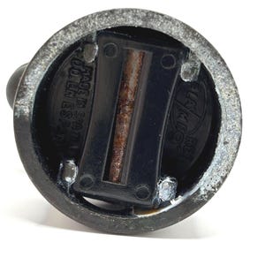 May include: Close-up of a dark metal bottle stopper. The stopper has a circular base with a black plastic insert and a small, rounded handle. The text "MADE IN SPAIN" is visible on the base.