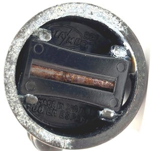 May include: Close-up of a vintage pencil sharpener. The sharpener is black with a rusty blade and is housed in a metallic casing. The text "PLAY ME" and "MADE IN SPAIN" are visible.