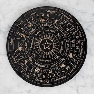 Peut inclure: Un plateau de divination noir avec des textes et symboles dorés. Le plateau circulaire présente des mois, des jours, des chiffres, des lettres et des symboles du zodiaque. Un motif central d'étoile et de soleil est présent. Les mots "Yes", "No" et "Check Again" sont également inclus.