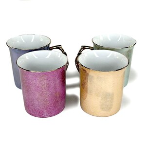 May include: Four ceramic mugs with gold-colored handles and rims. The mugs have a metallic finish in shades of purple, gold, blue, and green. The interior of each mug is white.