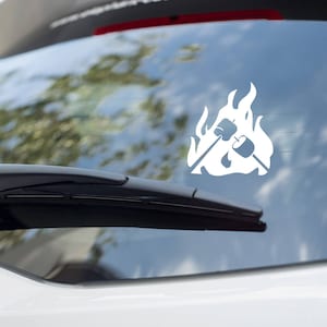 May include: White vinyl decal of a campfire with two marshmallows on sticks. The decal is on the back window of a car.