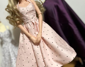 May include: A pink dress with black polka dots. The dress has a halter neckline and a full skirt. The dress is made of a soft, lightweight fabric.