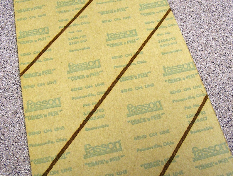 May include: A rectangular sheet of tan backing paper with repeating green text that reads Fasson Crack 'n Peel, Send on Line, Painesville, Ohio, and patent numbers 3,006,793 and 3,005,957. Two dark brown diagonal lines cross the paper surface.