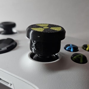 May include: A white Xbox controller with a black and yellow radiation symbol thumbstick cover.