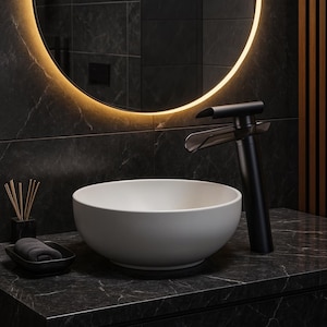May include: A contemporary bathroom scene with a white, circular basin and a stylish black tap. The tap has a distinctive design with a curved spout. A black soap dish and a lit mirror complete the modern aesthetic.