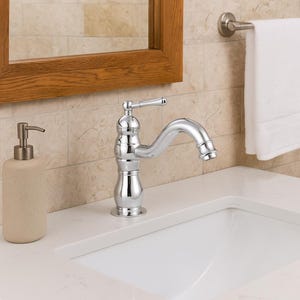 Puede incluir: Un grifo de baño cromado con un caño curvo y manija de palanca está montado en una encimera blanca. También se ven un dispensador de jabón beige y una toalla blanca. El grifo tiene un diseño clásico.