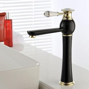Puede incluir: Un grifo de baño alto con acabado en negro brillante y detalles en tono dorado. La manija es blanca con un delicado patrón floral y borde dorado. El diseño incluye un caño curvo y una base cilíndrica, logrando una apariencia elegante.