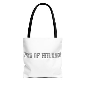 May include: White tote bag with black handles featuring the text "BAG OF HOLDING" in a black, blocky font. The bag is made of a white fabric and has a simple, clean design, suitable for carrying various items.
