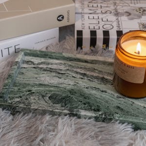May include: A green marble tray with a candle on top. The candle is in a clear glass jar with a brown label that says "Cedar & Moss".