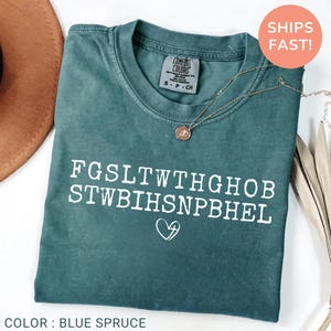 Pu&ograve; includere: T-shirt Comfort Colors blu abete con testo bianco e un cuore con una croce. Una collana d'oro con un ciondolo &egrave; sulla maglietta. La maglietta ha un girocollo e maniche corte. La maglietta &egrave; di taglia S.
