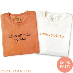 May include: Two folded t-shirts, one yam-coloured and one ivory, are displayed. The yam-coloured shirt has the text "kind of rude potato" in black, while the ivory shirt says "sweet potato" in orange. The shirts are labelled "Comfort Colors".